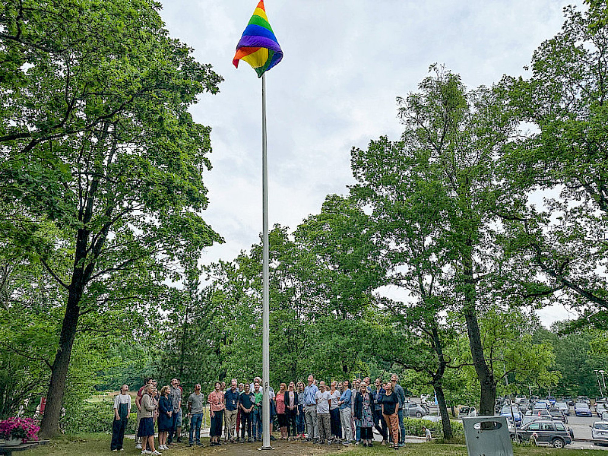 Ansatte har heiset pride flagget og står rundt flaggstangen og ser opp på flagget